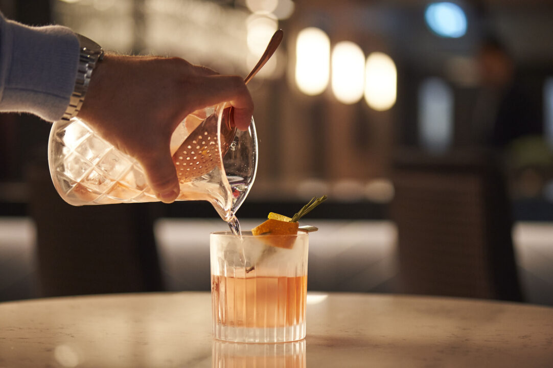 Someone pouring a Negroni into a glass