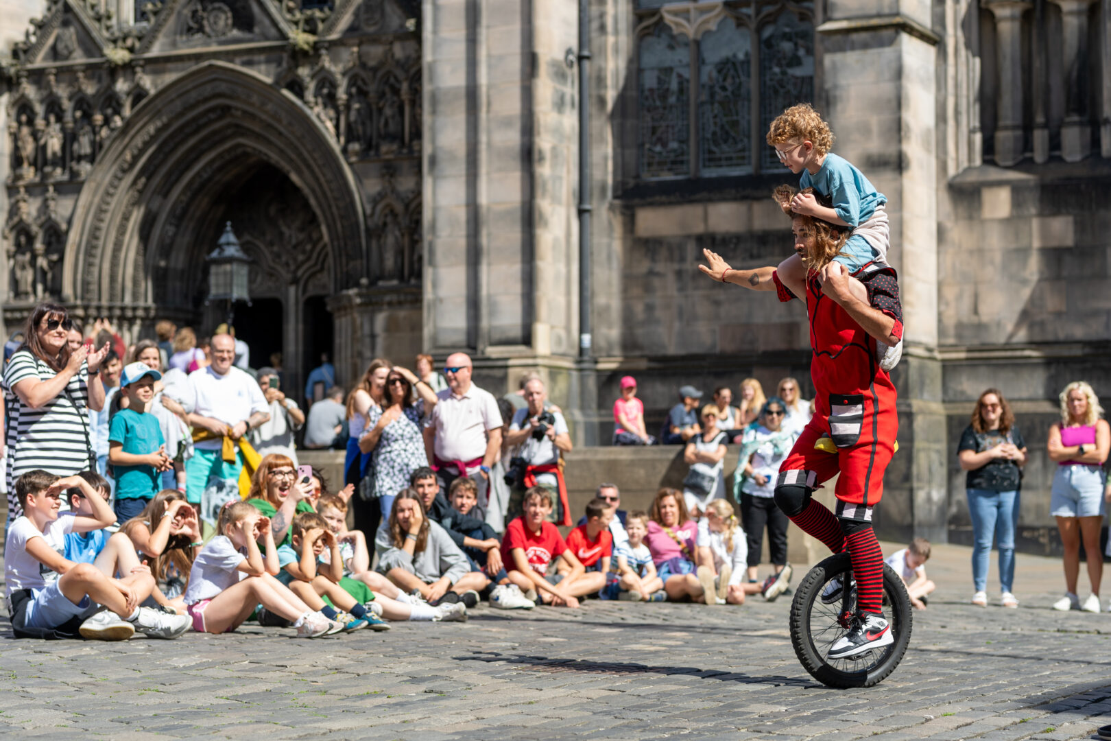 Man and child on unicycle in front of a crowd at Fringe