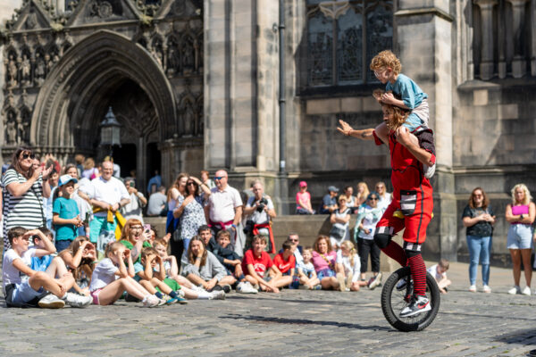 Man and child on unicycle in front of a crowd at Fringe