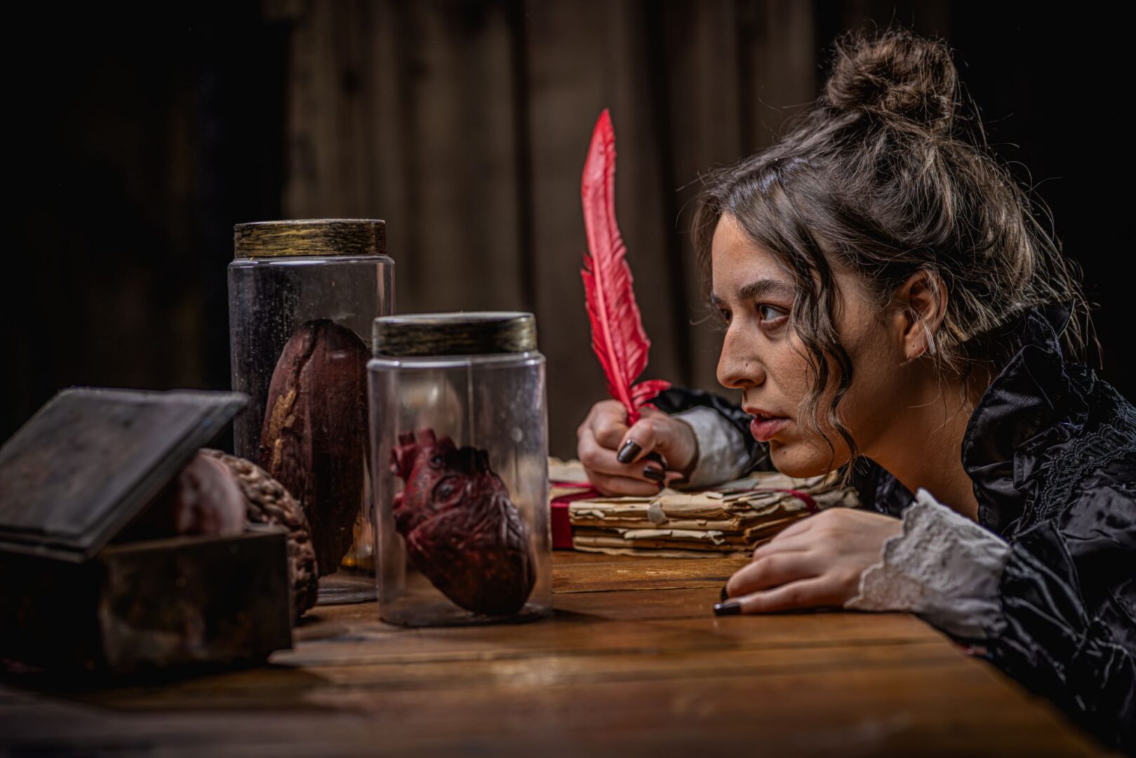 Close-up of a woman holding a feather pen and staring at jars with objects in them.