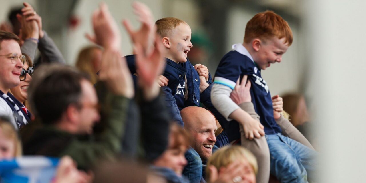 A crowd of people, focusing on 2 small boys being held up above the height of the crowd.