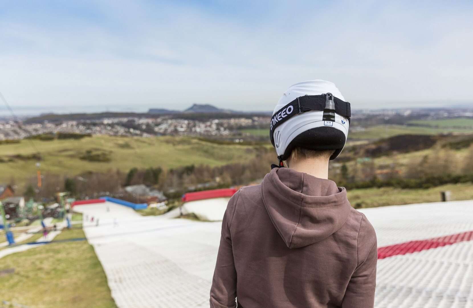 Skier staring down the dry ski slope at Hillend with Edinburgh skyline in distance