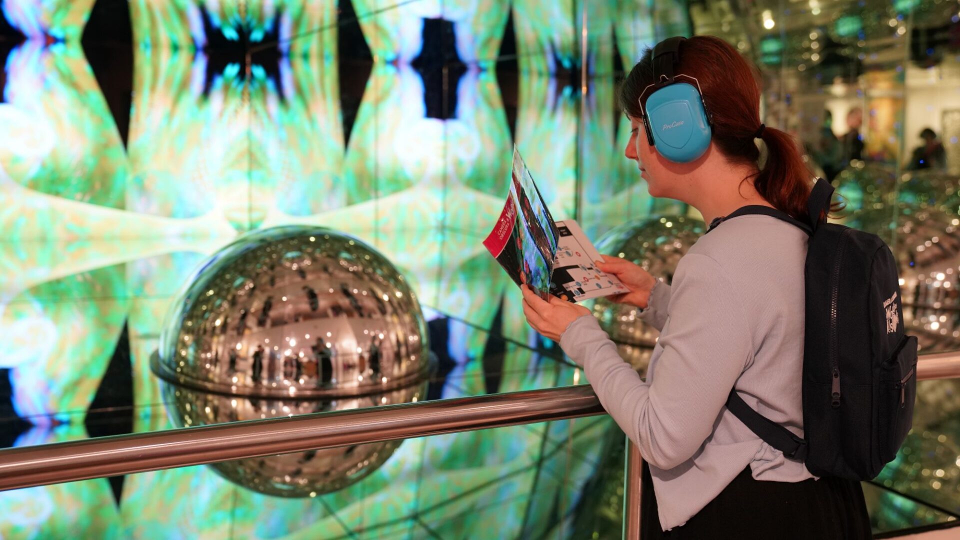 A girl with ear defenders looks at a sensory map in front of the Giant Kaleidosphere exhibit at Camera Obscura & World of Illusions, Edinburgh
