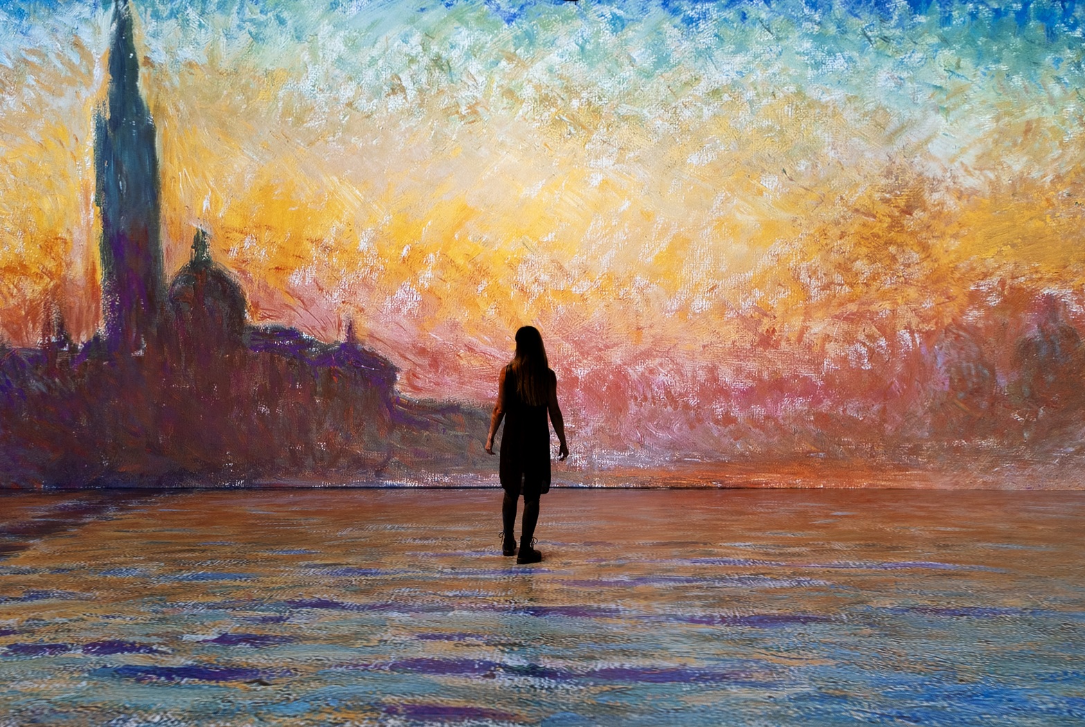 Women looking at a wall, on which is a projection of a painting of city skyline in shades of red, orange and blue.