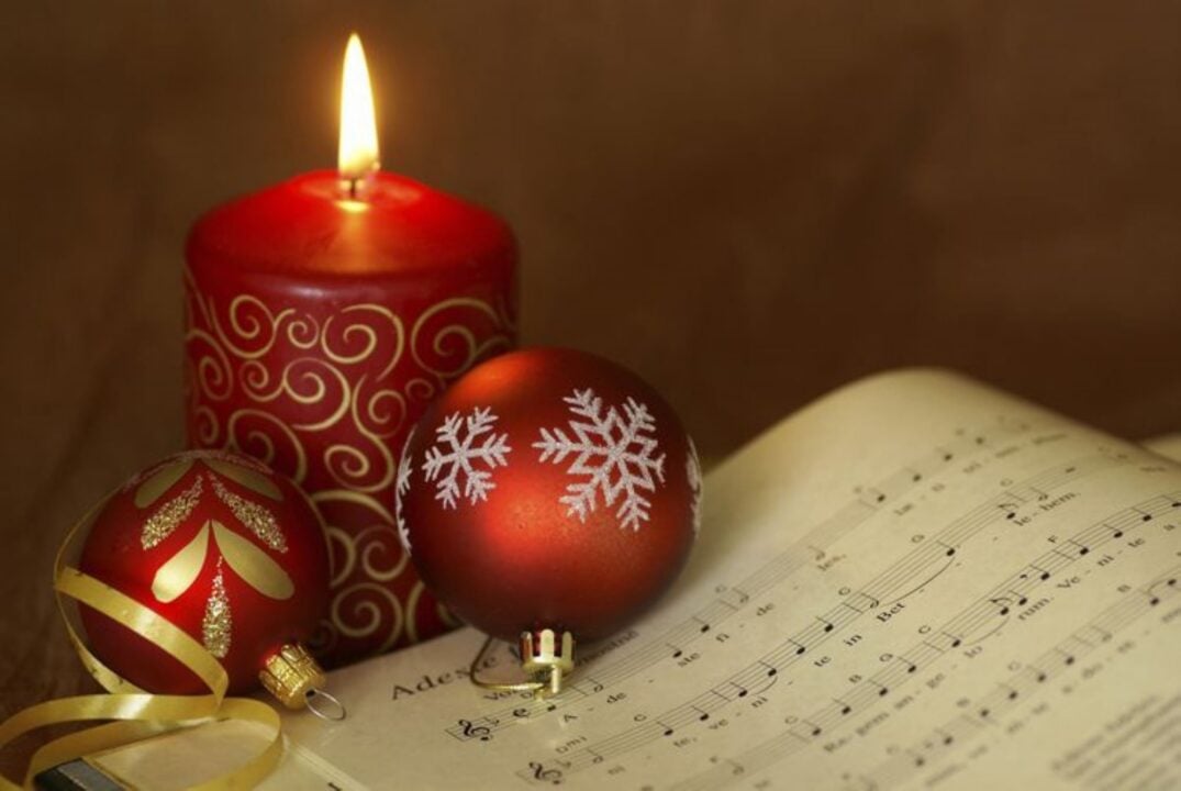 Close up of 2 red Christmas baubles, a candle and a sheet of music.