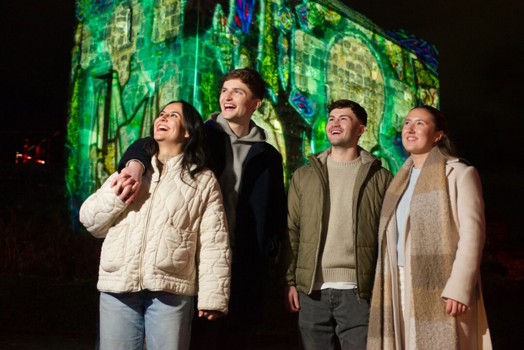 4 people standing outside, against the backdrop of a brightly lit building.