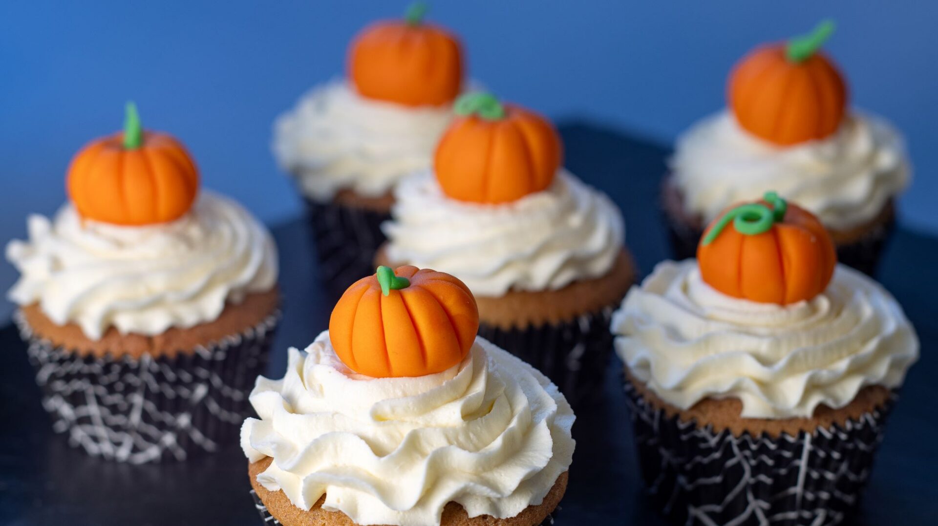 6 cupcakes with white icing and orange pumpkin toppers.