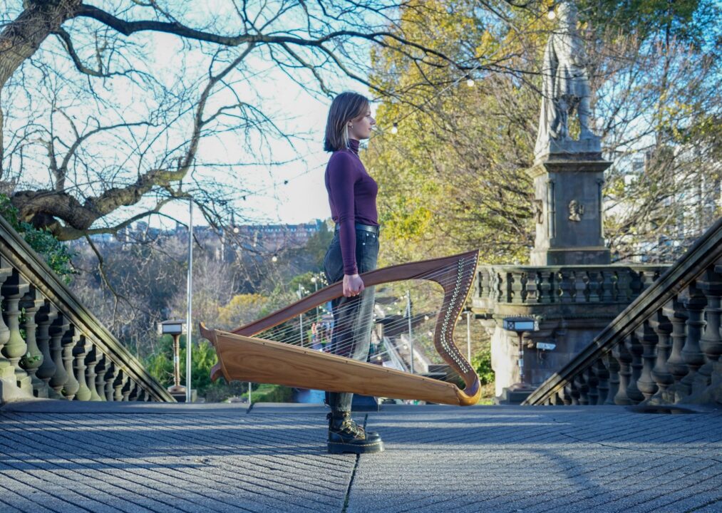 Women standing at the top of a series of stone steps outside, holding a harp.