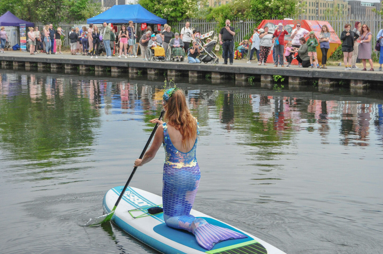 A woman dressed as a mermaid rowing on a paddleboard