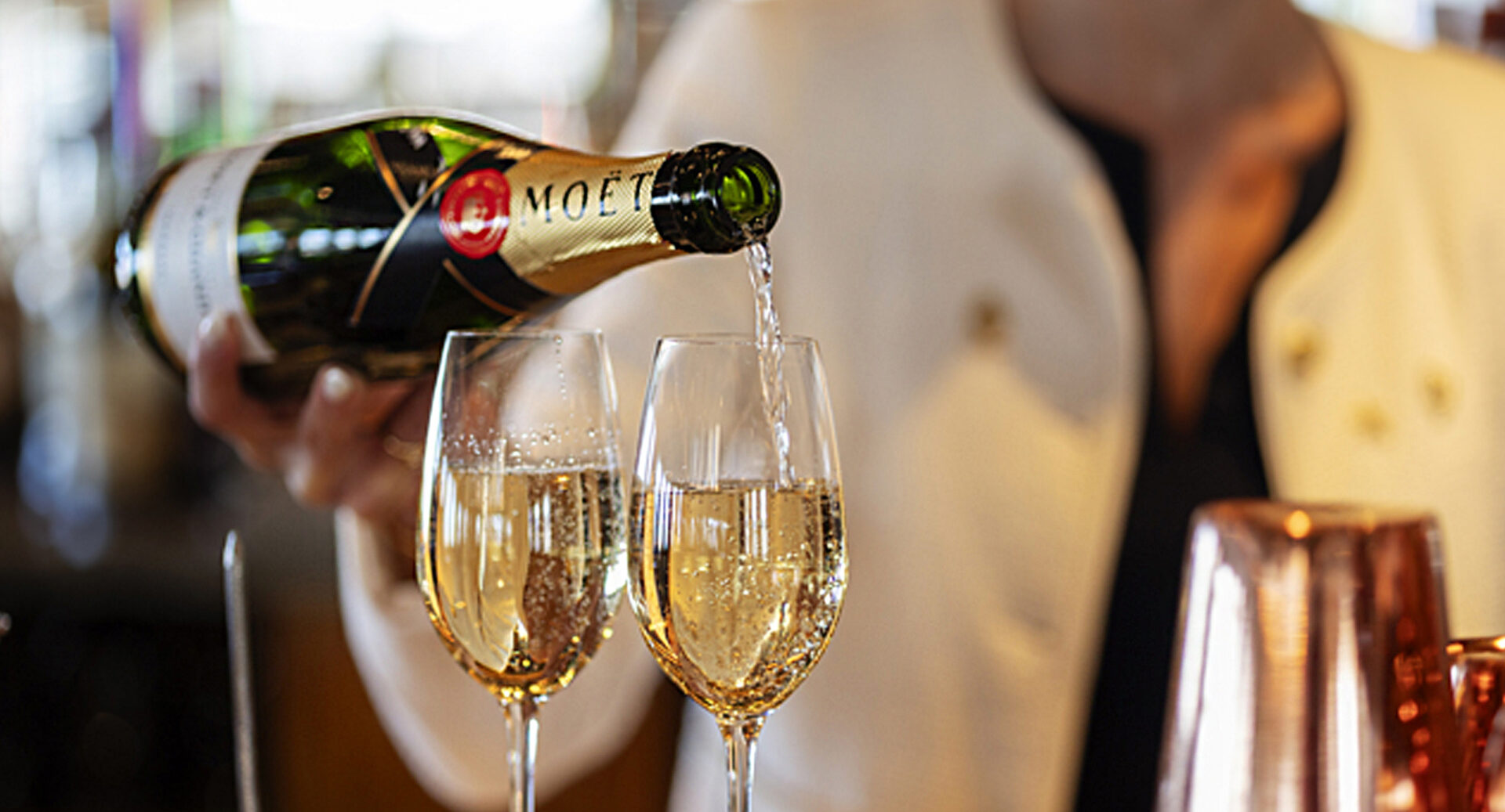Close-up of someone pouring a bottle of champagne into 2 glasses.