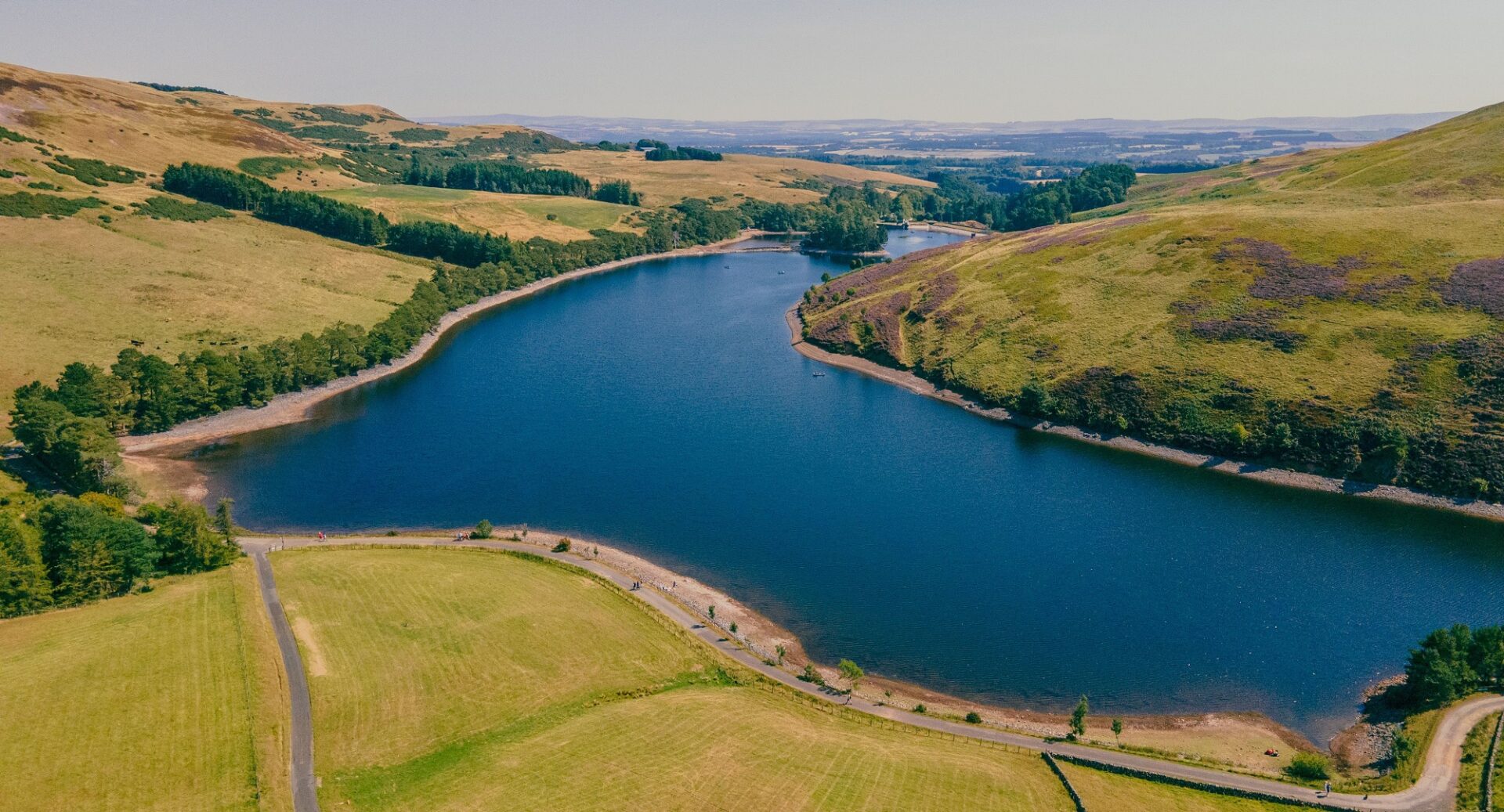 Beautiful shot of the Glencorse Reservoir surrounded by green trees and land