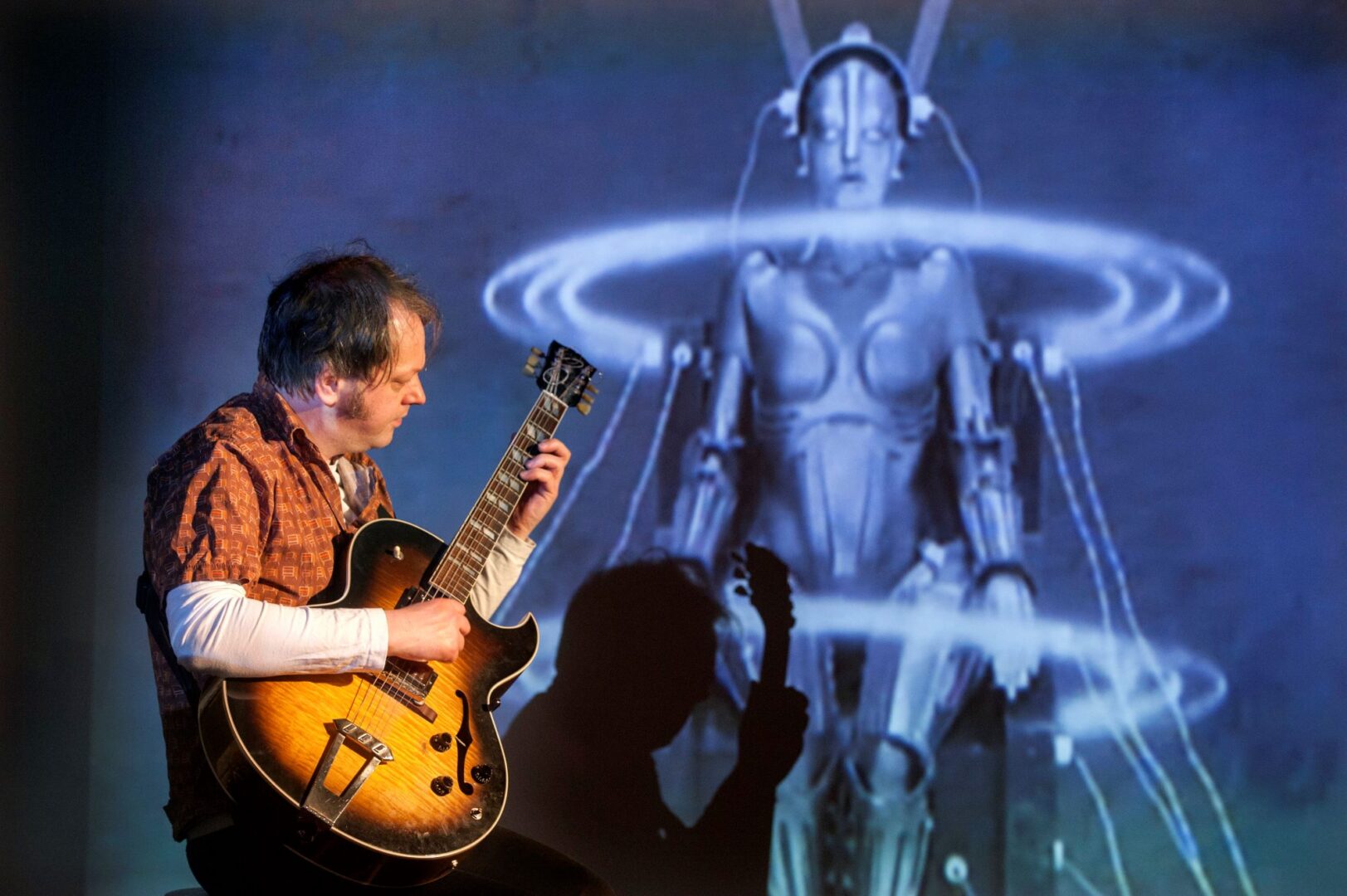 Man playing a guitar, with an image of a robot in the background.