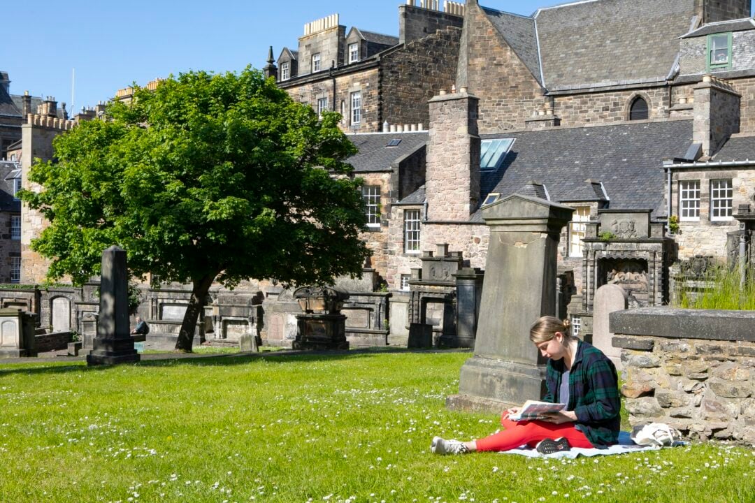 A woman sitting reading on the grass in Greyfriars Kirkyard