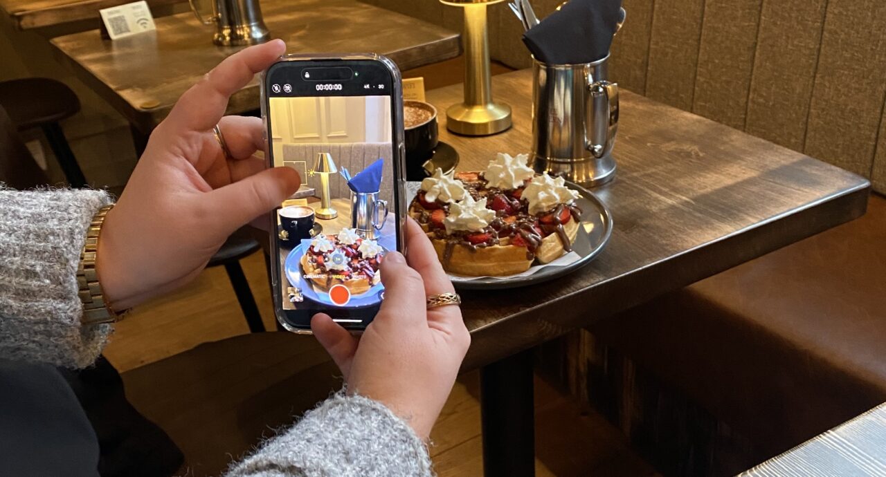 Hand holding phone with image of Waffles with Strawberries and Chocolate Sauce