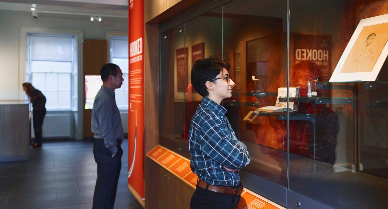 2 people looking at display of items, inside a glass cabinet.