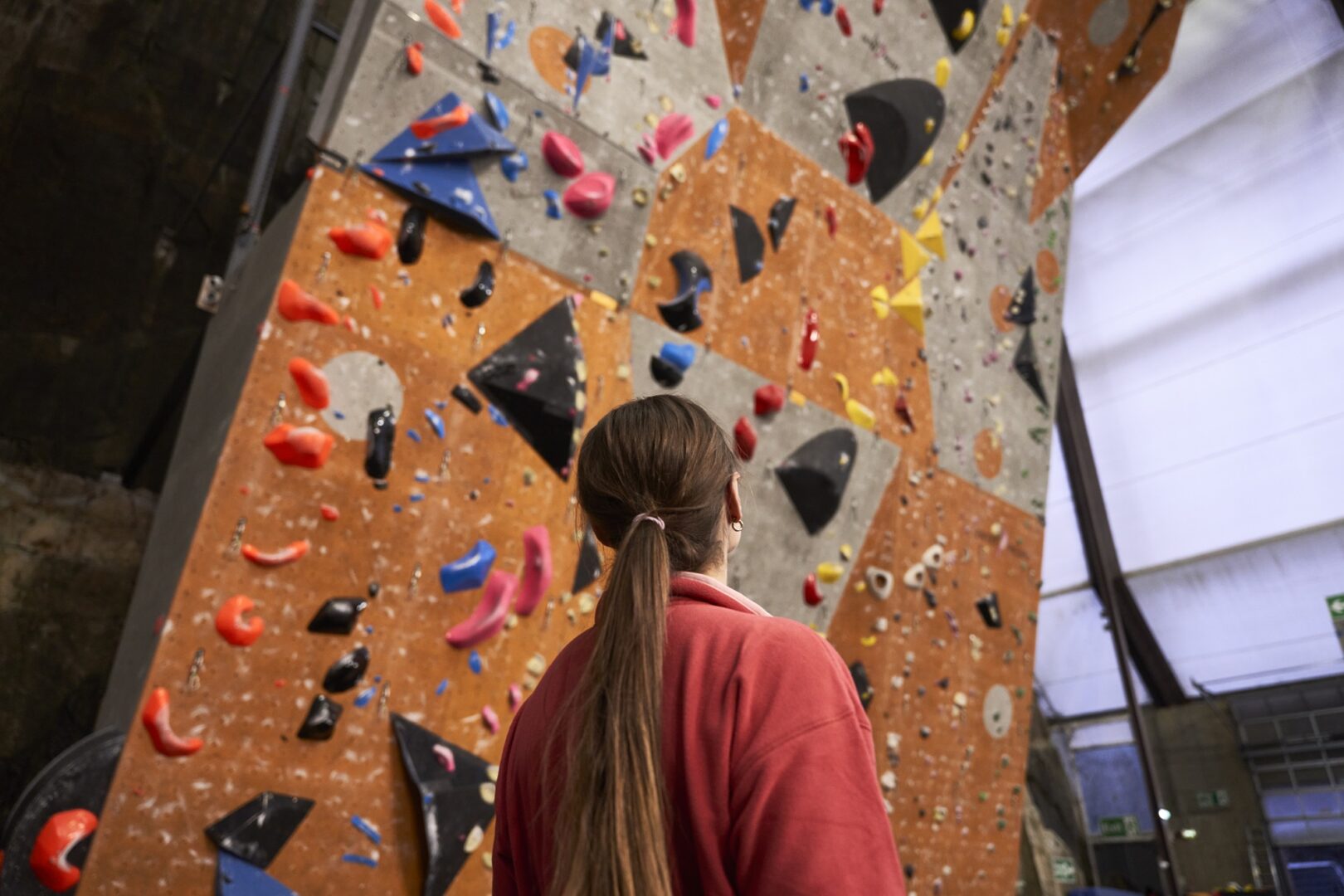 Lady staring up the face of an indoor Rock Climbing Wall