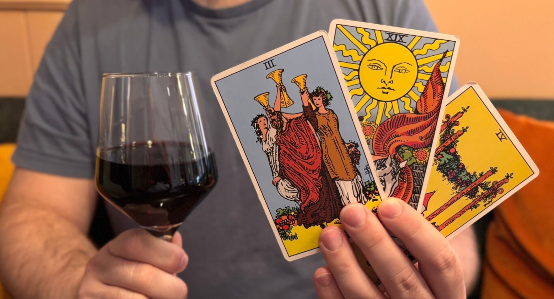 A person holding a set of tarot cards and a glass of dark red wine.