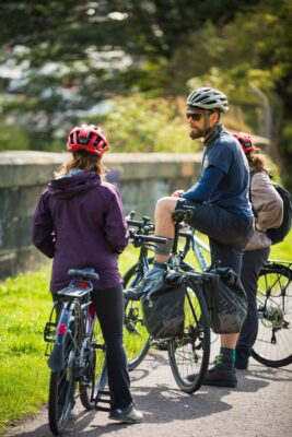 Man standing next to his bike speaking to two other bike riders.