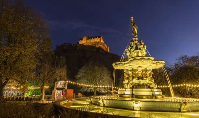 Ross-fountain lit up in gold light with castle in background.