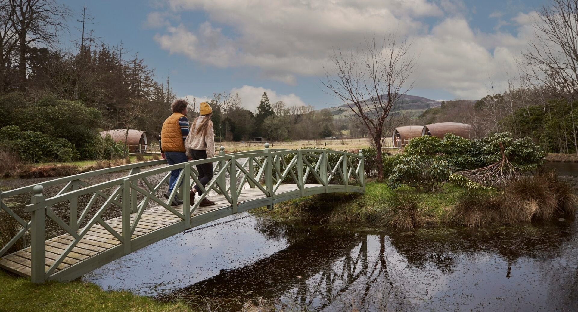 man and woman crossing bridge on way to glamping pod
