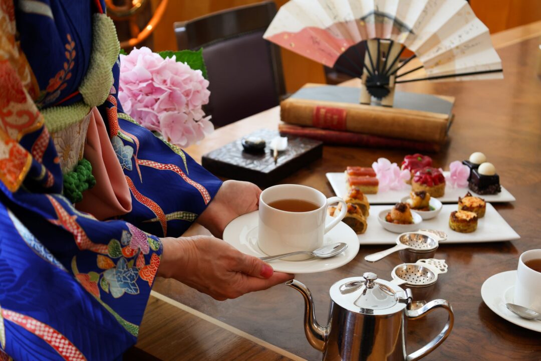 Close-up of person in traditional Japanese dress serving tea and small cakes.
