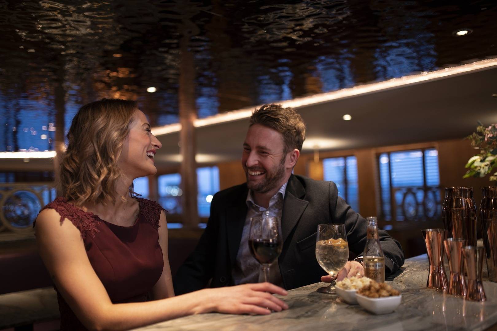 A man and a woman sit at the bar in The Lighthouse Restaurant & Bars smiling and laughing as they enjoy drinks under the shimmering ceiling. ,© Jeremy Rata