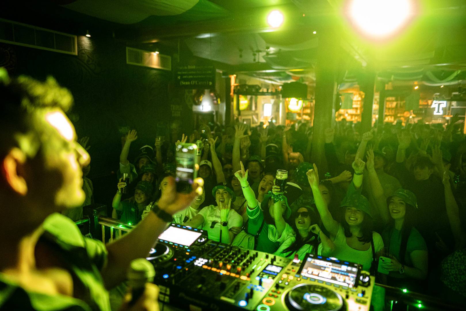 DJ takes a photo of the crowd waving their arms in the air on his phone,© Malones Edinburgh