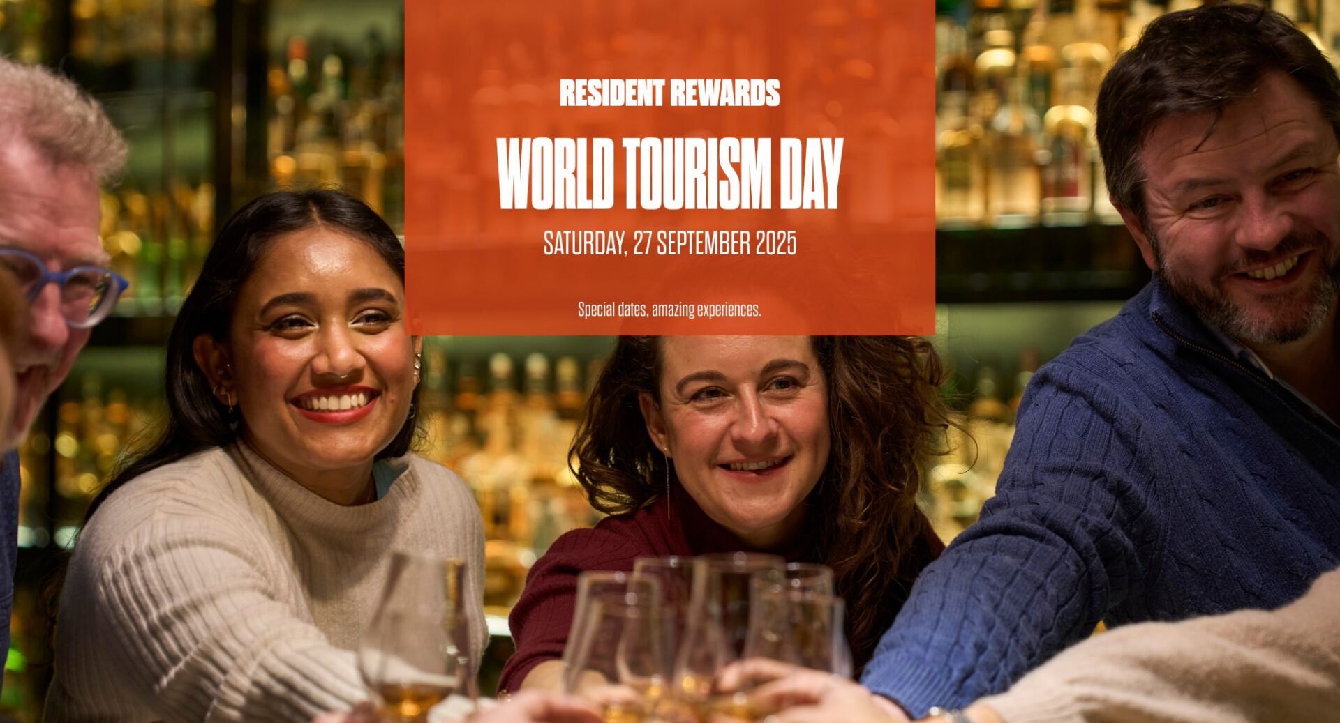 Group of people saying cheers and orange box with writing saying for World Tourism Resident Day